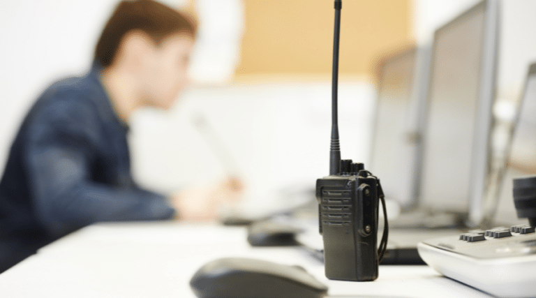 Talkie-walkie posé sur un bureau, avec une personne floue au second plan travaillant sur un ordinateur